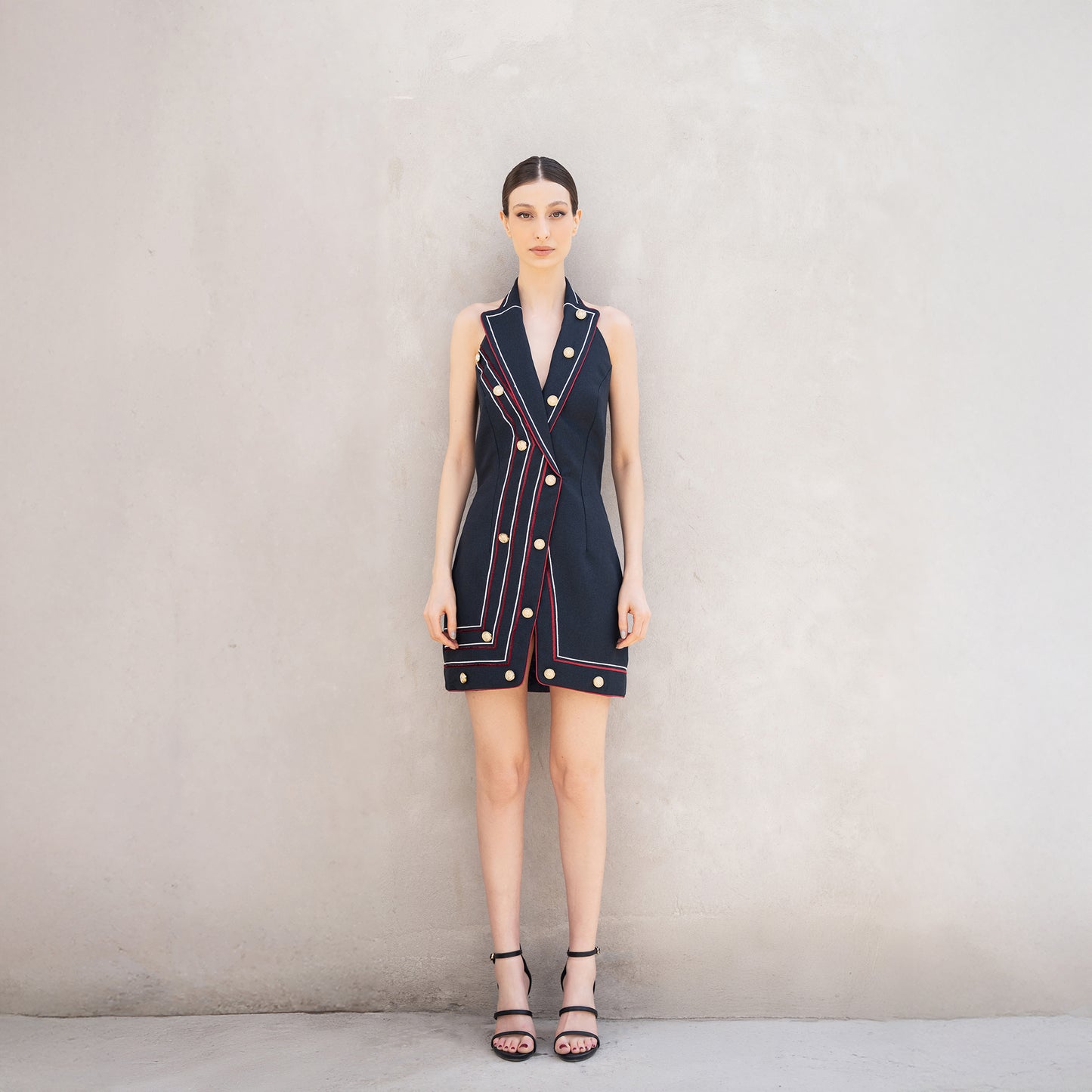 A woman wearing the Pulse dress, a sleeveless tailored dress made of Fastoni fabric with red and white laser-cut lines and golden buttons.