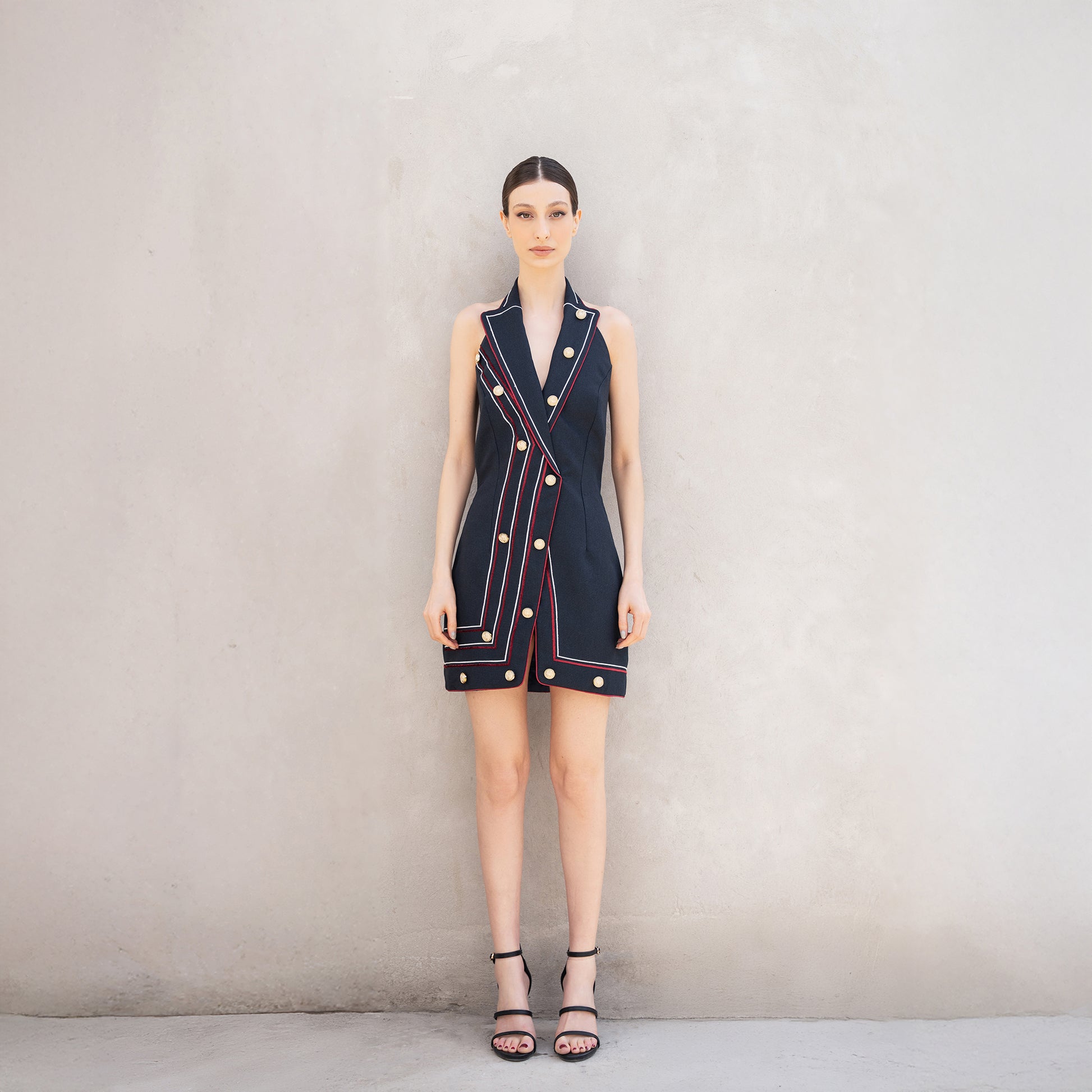 A woman wearing the Pulse dress, a sleeveless tailored dress made of Fastoni fabric with red and white laser-cut lines and golden buttons.