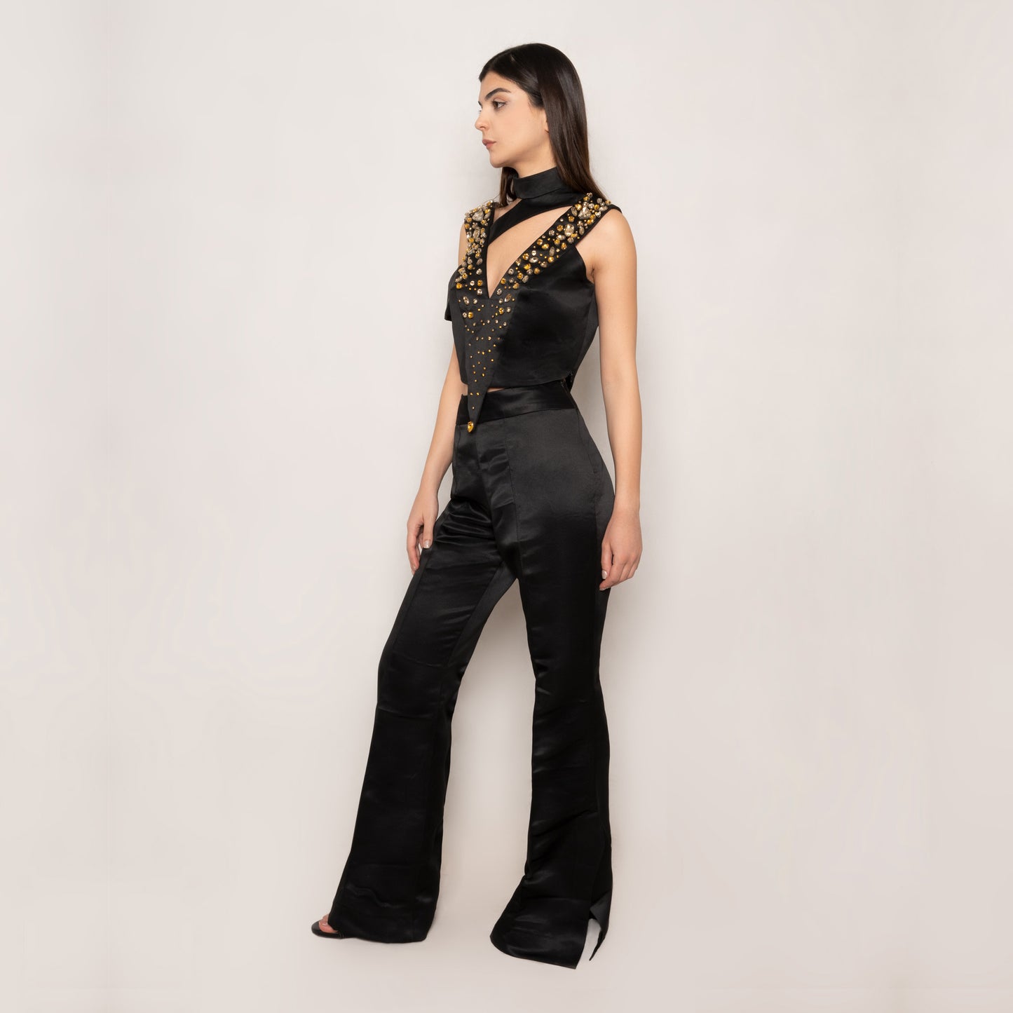 Side view of the Amber Essence Silk Set by Tehran, showcasing the elegant drape of premium black silk adorned with amber and champagne gold rhinestones. Features an asymmetric hem, short sleeves, and high-waisted flared pants with a tailored fit.