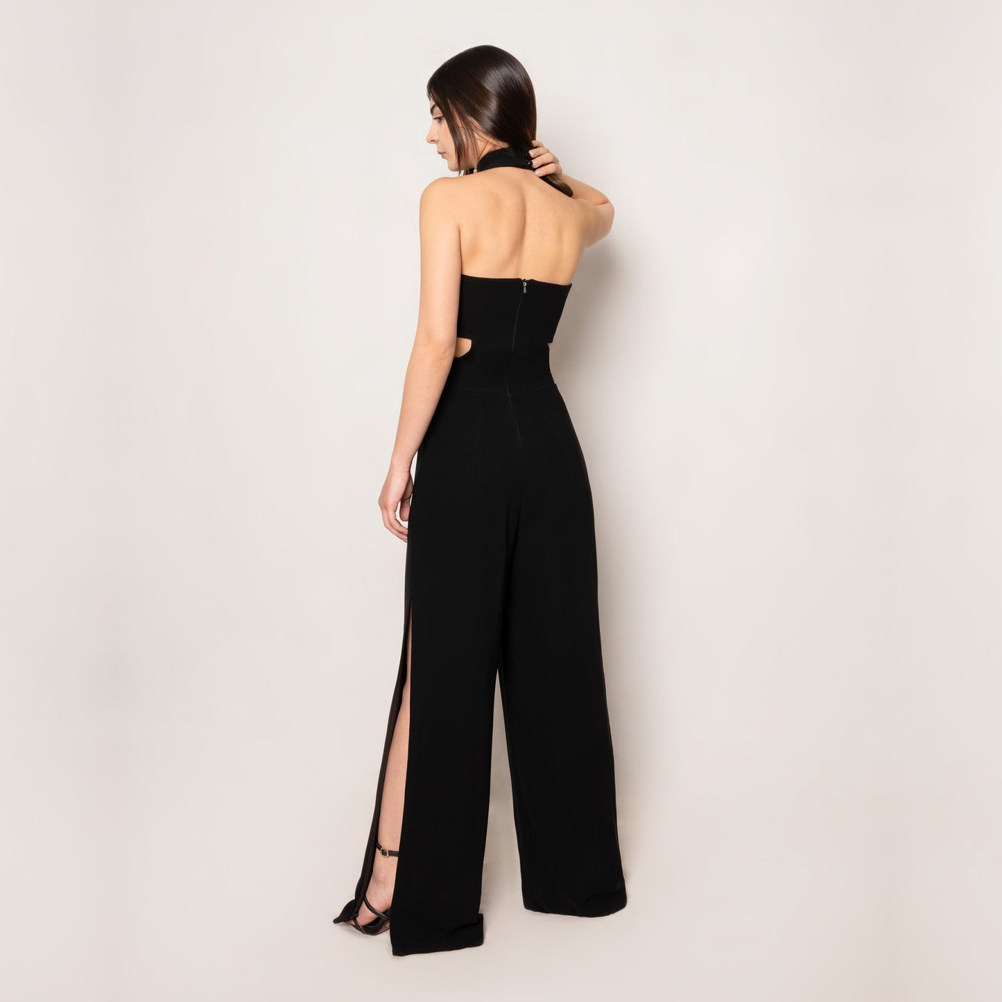 Back view of the Crystal Jumpsuit by Tehran, showcasing the sleek halterneck style and smooth black fabric. The tailored fit emphasizes timeless elegance with modern detailing.