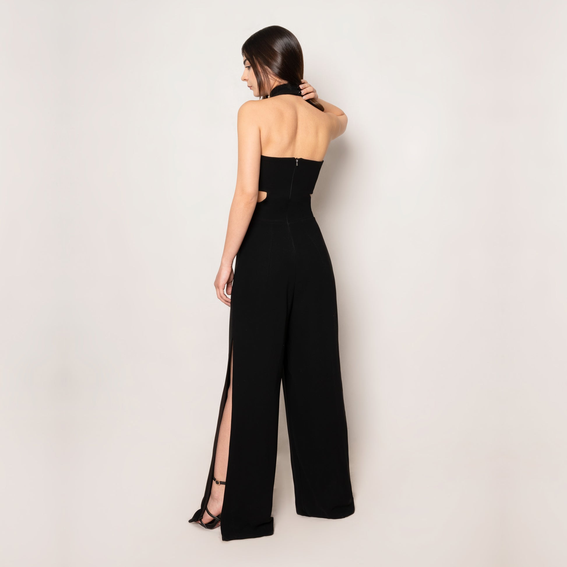 Back view of the Crystal Jumpsuit by Tehran, showcasing the sleek halterneck style and smooth black fabric. The tailored fit emphasizes timeless elegance with modern detailing.