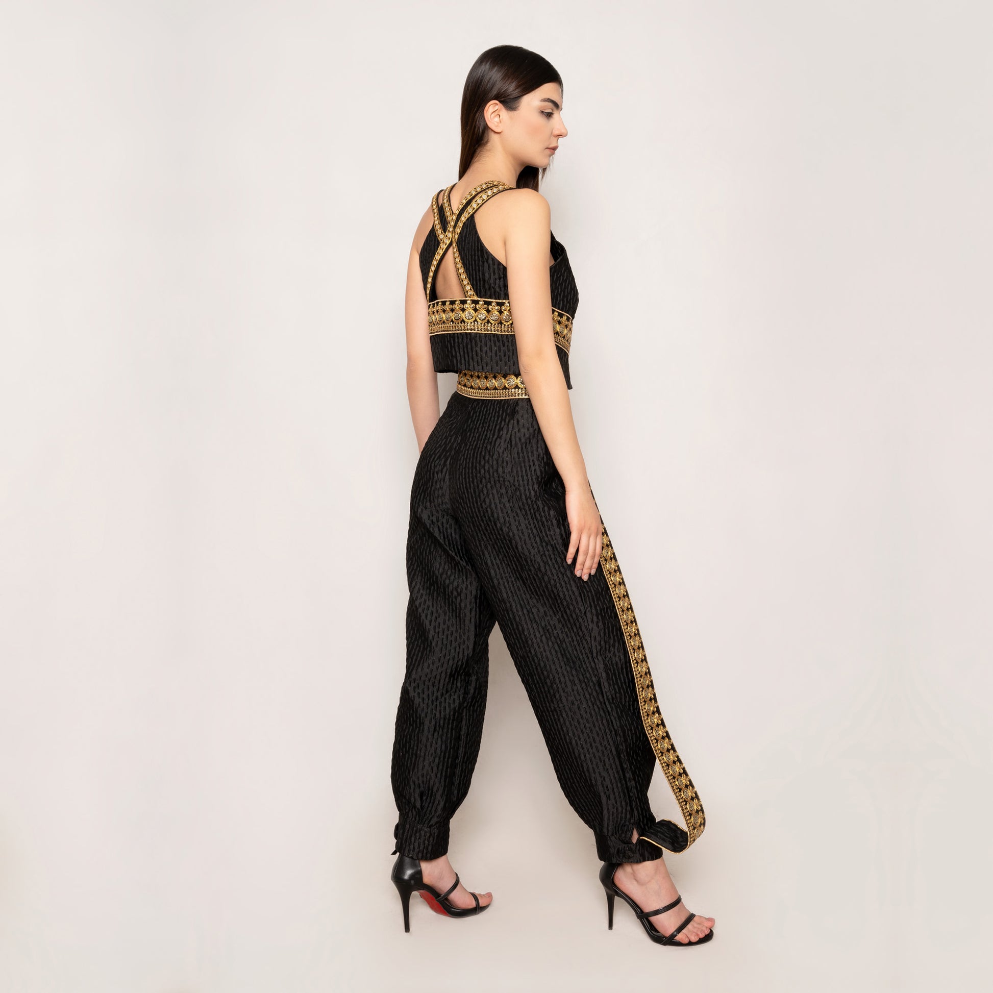 Side view of the Golden Nomad Set by Tehran in black, showcasing the sleeveless vest's elegant trims and the plunging V-neckline. The tapered pants with elasticated ankles and concealed zip fastening contribute to a tailored yet comfortable fit, emphasizing effortless style.