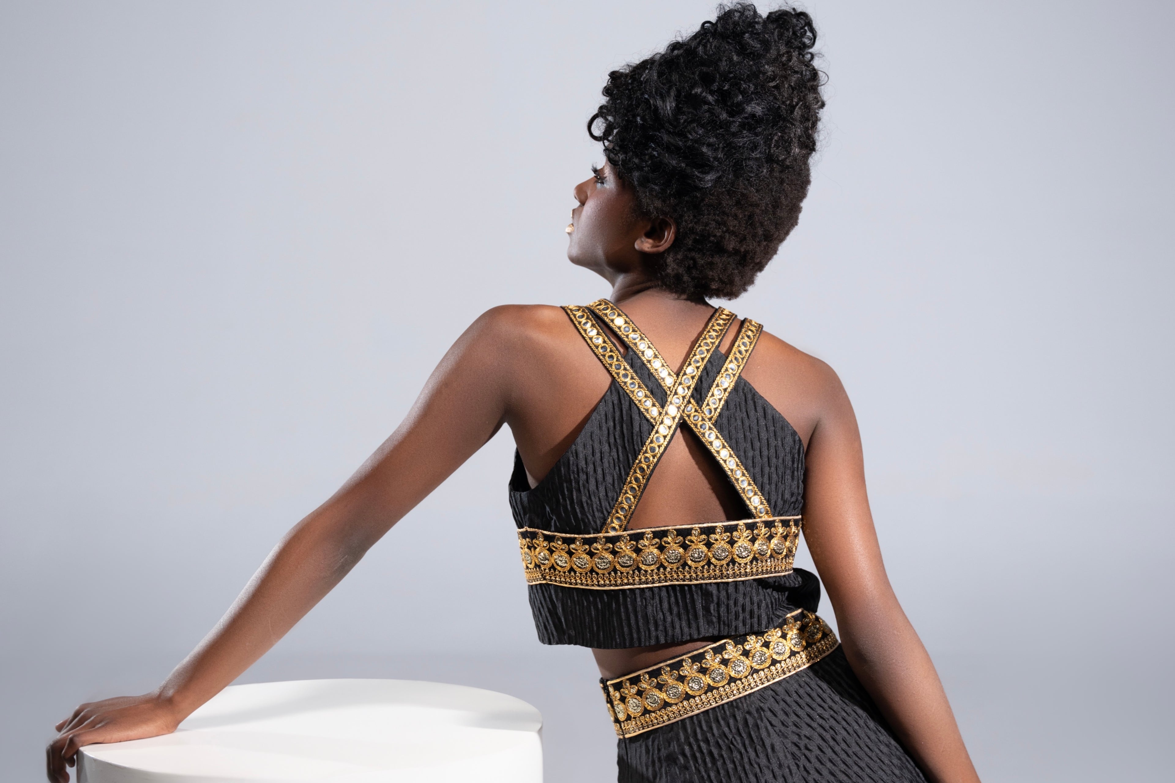 Back view of the Golden Nomad Set by Tehran, showcasing a luxurious black jacquard vest featuring elegant golden trims, intricate embellishments, and a keyhole detail. The sleeveless design highlights the structured fit and sophisticated craftsmanship. Model's back emphasizes the cross-strap pattern with detailed gold accents, exuding bold and modern elegance.