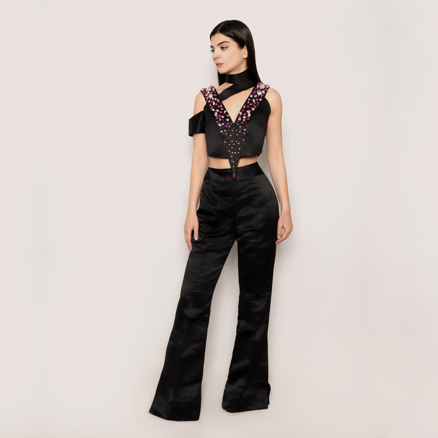 Front view of the Rose Essence Set by Tehran, featuring a black silk top adorned with light pink and magenta rhinestones, a plunging V-neckline, and an asymmetric design. Paired with high-waisted flared pants for a sleek and elegant evening look.